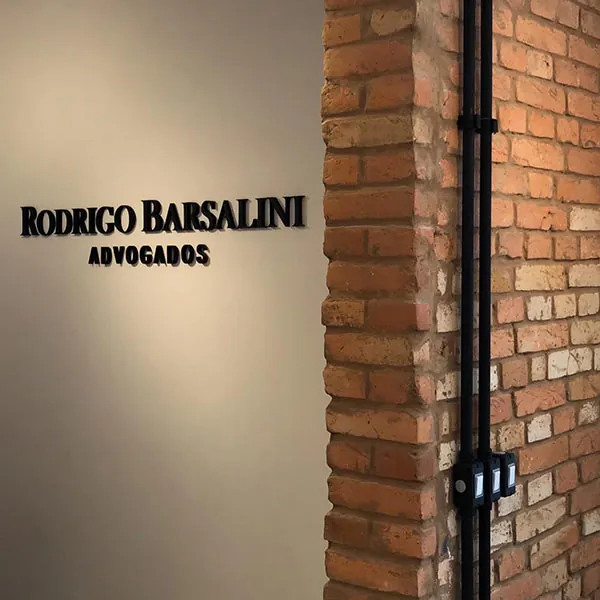 Parede da entrada com o nome Rodrigo Barsalini Advogados, ao lado de uma coluna de tijolo aparente